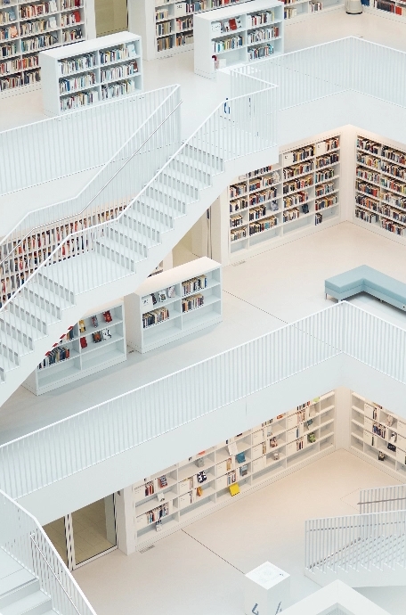 Blick von oben aus dem Treppenhaus in eine Bibliothek. Die Treppen, Regale und Fußböden sind weiß.